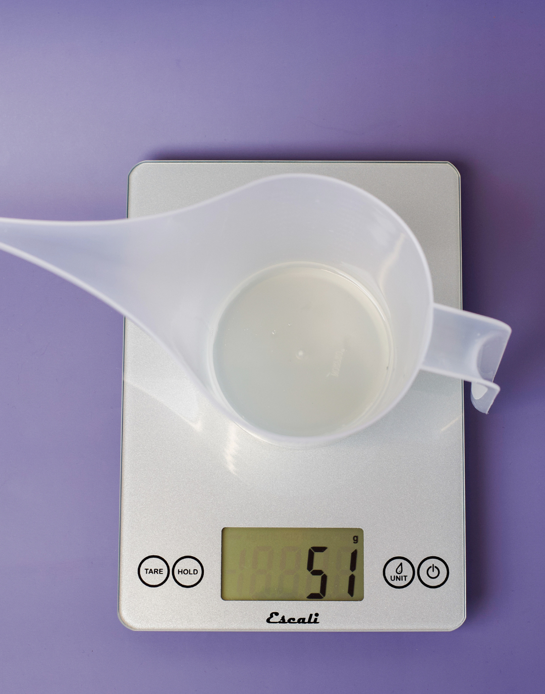 Funnel pouring pitcher containing room spray base on scale.